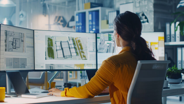 Architect reviewing blueprints on multiple screens in a modern design office.