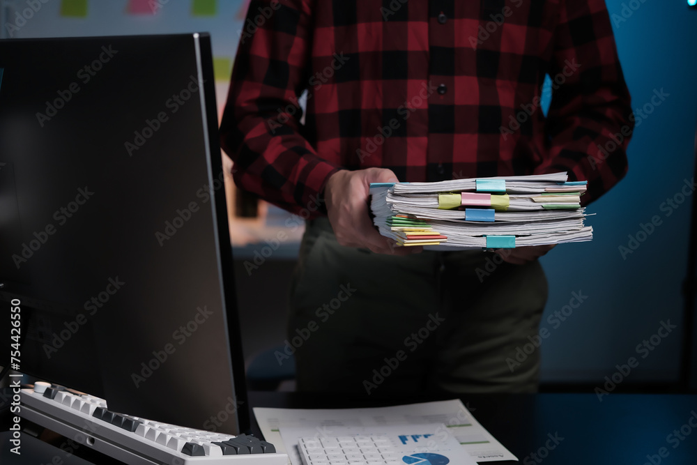 Poster A man is holding a stack of papers in front of a computer monitor