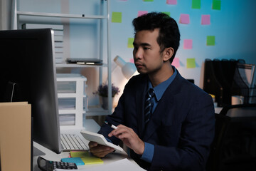 A man in a suit is sitting at a desk with a computer monitor and a tablet