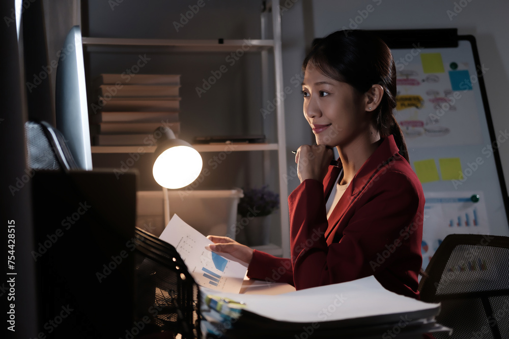 Poster A woman is sitting at a desk with a computer monitor and a stack of papers