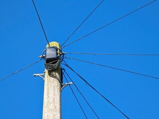 Wooden telegraph pole against a blue sky with cables routeing off in all directions connecting...