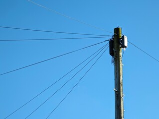 Wooden telegraph pole against a blue sky with cables routeing off in all directions connecting...