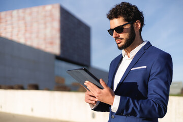 Successful and stylish executive manager using digital tablet in modern outdoors.