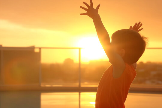 Young child raising hands in jubilation at sunset