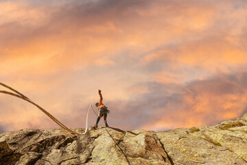 A woman is climbing a rock wall with a rope. The sun is shining on the rock wall, creating a...