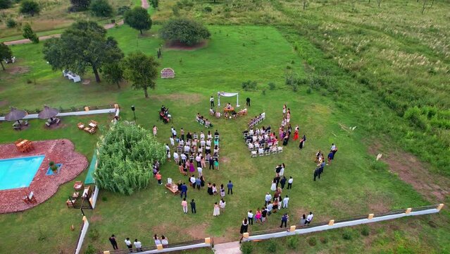 Top view of a wedding ceremony in a green field with guests and the newlyweds. The drone moves away and circles over the wedding venue on a green background...
