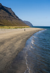 Girl walking alone on Holt sandy beach close to Önundarfjörður Pier in Westfjords, Iceland. Beautiful nature and travel destination