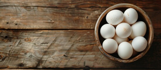 A wooden table hosts a bowl filled with white eggs. The simple and rustic setup showcases the purity of white eggs against the natural wood backdrop.