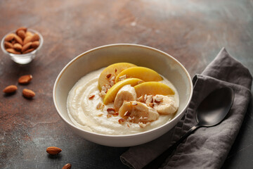 Sweet milky semolina porridge with apples bananas and almonds in a bowl on the table. Healthy children's breakfast.