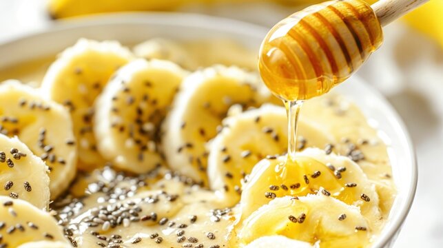 A close-up image of a smoothie bowl topped with sliced bananas, chia seeds, and a drizzle of honey, set against a bright, light background. The ingredients' textures and the smoothie's vibrant color a