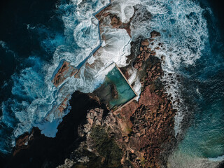 Obraz premium Aerial view early morning light with ocean waves flowing over rocks around North Curl Curl ocean rock pool during storm.