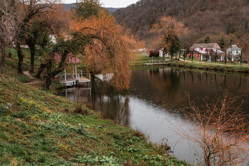 Fototapeta premium Beautiful natural landscape with a lake surrounded by trees. A cloudy day and a wooden gazebo. Pond in autumn, yellow leaves, reflection. A colorful landscape on a lake in the Caucasus forest. 