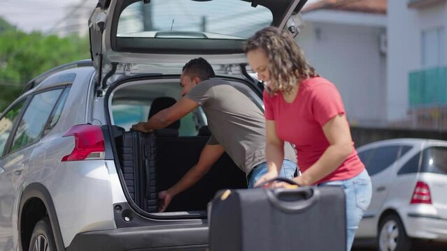 Happy couple puts his suitcase in the back of the car and prepares to leave for trip. Husband and wife open the back of the car put luggage travel. Couple moving into new home at moving day
