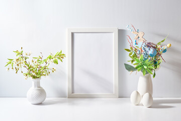 Mockup with a white frame and spring flowers in a vase, easter eggs on a light background. Empty poster frame mockup for presentation design, text, lettering