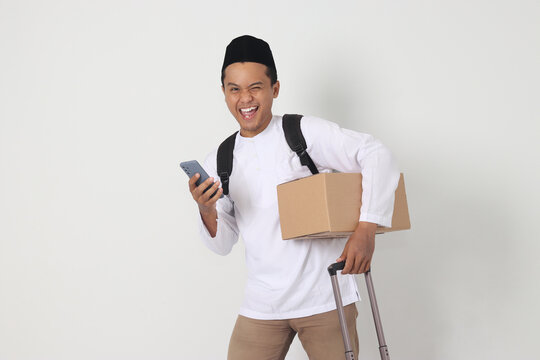Portrait of happy Asian muslim man carrying cardboard box and suitcase while holding mobile phone. Going home for Eid Mubarak. Isolated image on white background