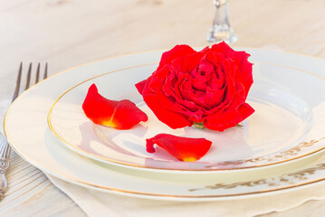 Romantic place setting for dinner: red rose on a white plates on a white napkin; close up