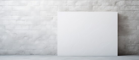 A white square blank piece of paper is seen taped to a white brick wall with beige plaster. The stark contrast between the white box and the brick wall creates a visually interesting composition - obrazy, fototapety, plakaty