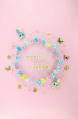 Easter celebration composition. Top view of a frame made of easter egg candies, small flowers isolated on pastel pink background. Easter concept. Flat lay, top view, copy space