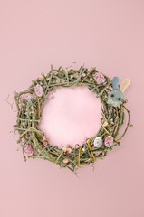 Wreath of branches on pink background with colorful easter egg candies, flowers and bunny figures. Easter concept.