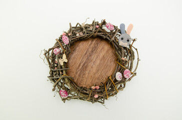 Wreath of branches on wooden plate on beige background with colorful easter egg candies, flowers and bunny figures. Easter concept.