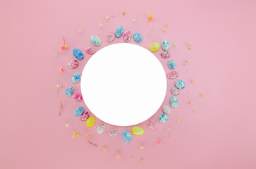 Easter celebration composition. Top view of blank white circle, easter egg candies, small flowers isolated on pastel pink background. Easter concept. Flat lay, top view, copy space