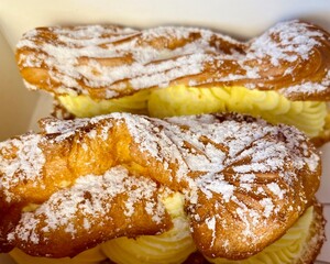 close in a cardboard box lie two eclairs with custard sprinkled with powdered sugar. side view, sweets