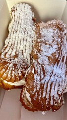 in a cardboard box there are two eclairs with butter cream sprinkled with powdered sugar. high-calorie sweets