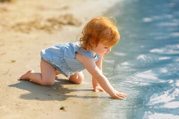 Red hair baby girl sits on the sand on the beach in summer. Exploring toddler: beachside adventures 