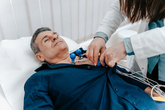 Experienced doctor putting electrodes of a ECG machine on the bare torso of a senior male patient. At the Emergency ward of a hospital.