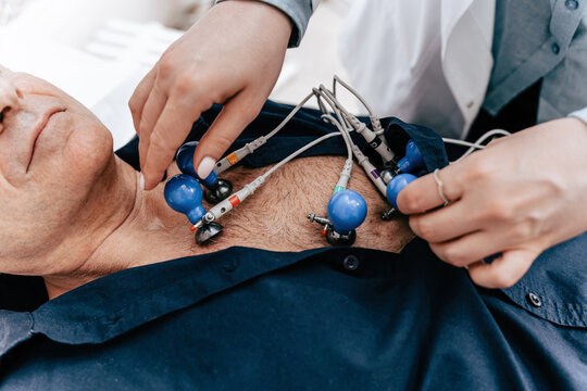 Experienced doctor putting electrodes of a ECG machine on the bare torso of a senior male patient. At the Emergency ward of a hospital. Close up shot.