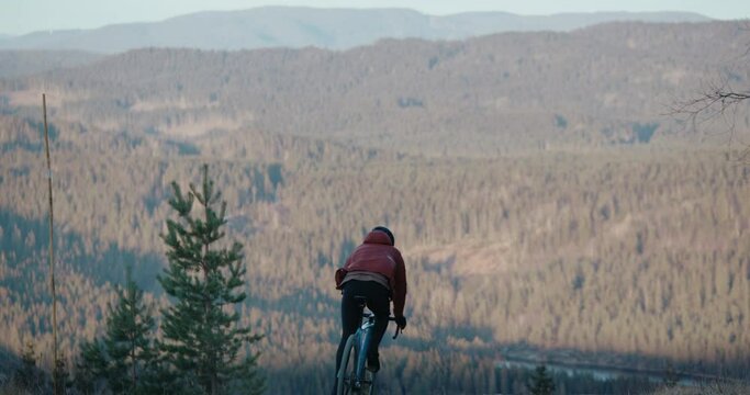 Cyclist ride down gravel road on carbon cyclocross bike, overlook forest and mountains. Fast and skilled professional cyclist during adventure bikepacking offroad ride