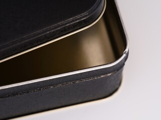 A close-up shot of an empty open black tin box of cookies on a white background