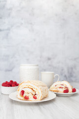 Meringue roll with strawberries and raspberries on white wooden table.  