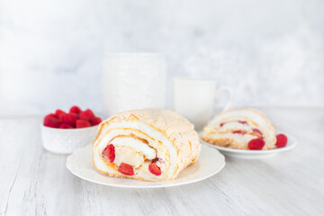 Meringue roll with strawberries and raspberries on white wooden table.  