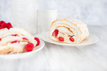 Meringue roll with strawberries and raspberries on white wooden table.  