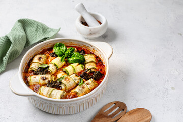 Italian zucchini rolls with cream cheese filling, baked in tomato sauce on a white background.