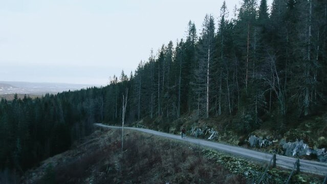 Cinematic drone shot of cyclist descend picturesque epic gravel road in norwegian mountain surrounded by forest. Beautiful and inspiring off road cycling destination