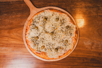 Overhead view of a cheese pizza with olives on a wooden bar table.