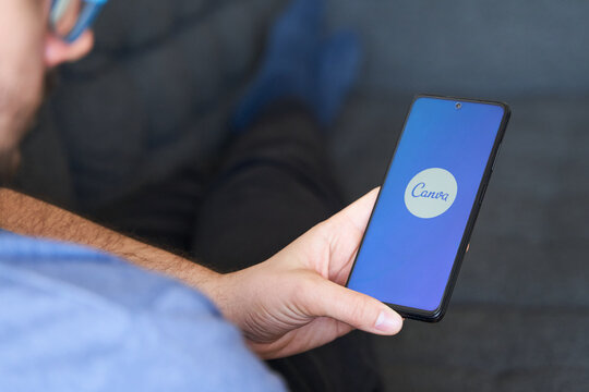 Young male in sofa using Canva app in  smartphone
