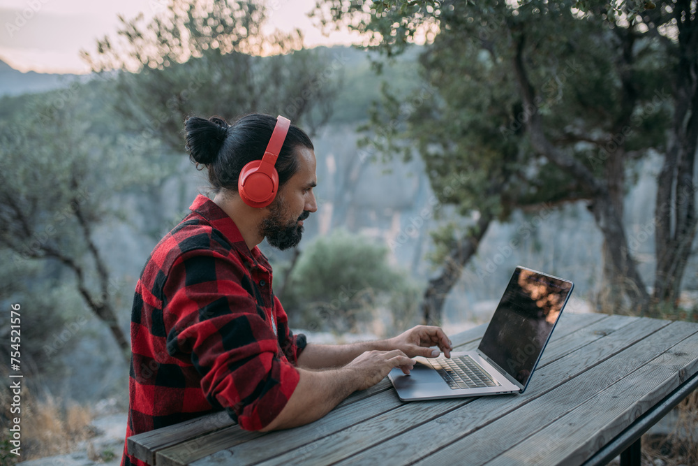 Wall mural A young man is working on a laptop at a camping site in the mountains.