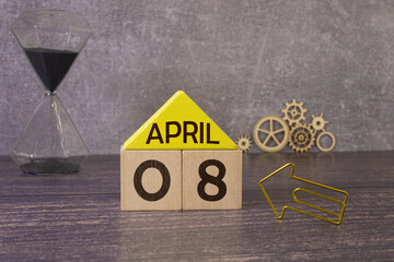 April 08 calendar date text on white wooden block with stationeries on wooden desk.