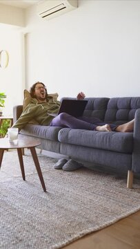 Vertical shot of young man waking up after nap with laptop on the sofa