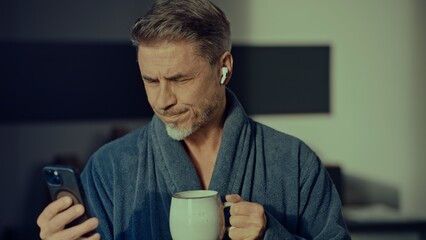 Happy man in bathrobe with phone at home in morning