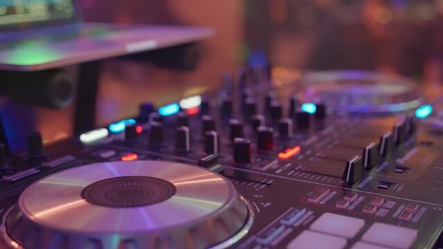 Exciting footage of a DJ playing music on a mixer, controller, and turntable in a club setting. Closeups of equipment with CDs on them create a vibrant and energetic atmosphere