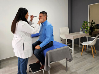 Latin woman doctor specialist ophthalmologist checks the eyes of her dark-skinned male patient...