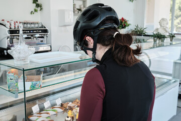 A woman cyclist, wearing full cycling gear, is going to eat buns and drink coffee after a hard ride on her bicycle in a cozy cafe. Healthy lifestyle concept. Cycling adventure. 