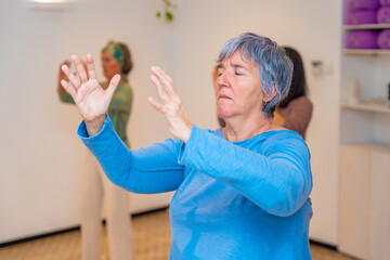 Elder woman closing eyes and raising arms during qi gong class
