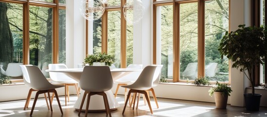 Fototapeta premium A dining room featuring a white round table surrounded by creative chairs, illuminated by natural daylight streaming in from large windows. Above,