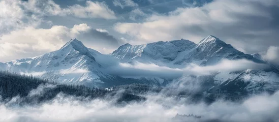 Papier Peint photo Tatras The rugged mountain range stands tall, covered in a blanket of snow and surrounded by dense clouds.