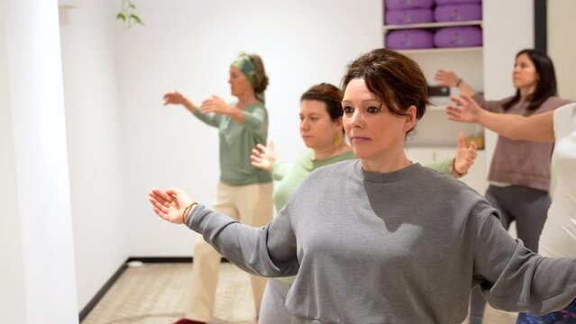 Group of mature adult and caucasian sportive women opening arms during qi gong class